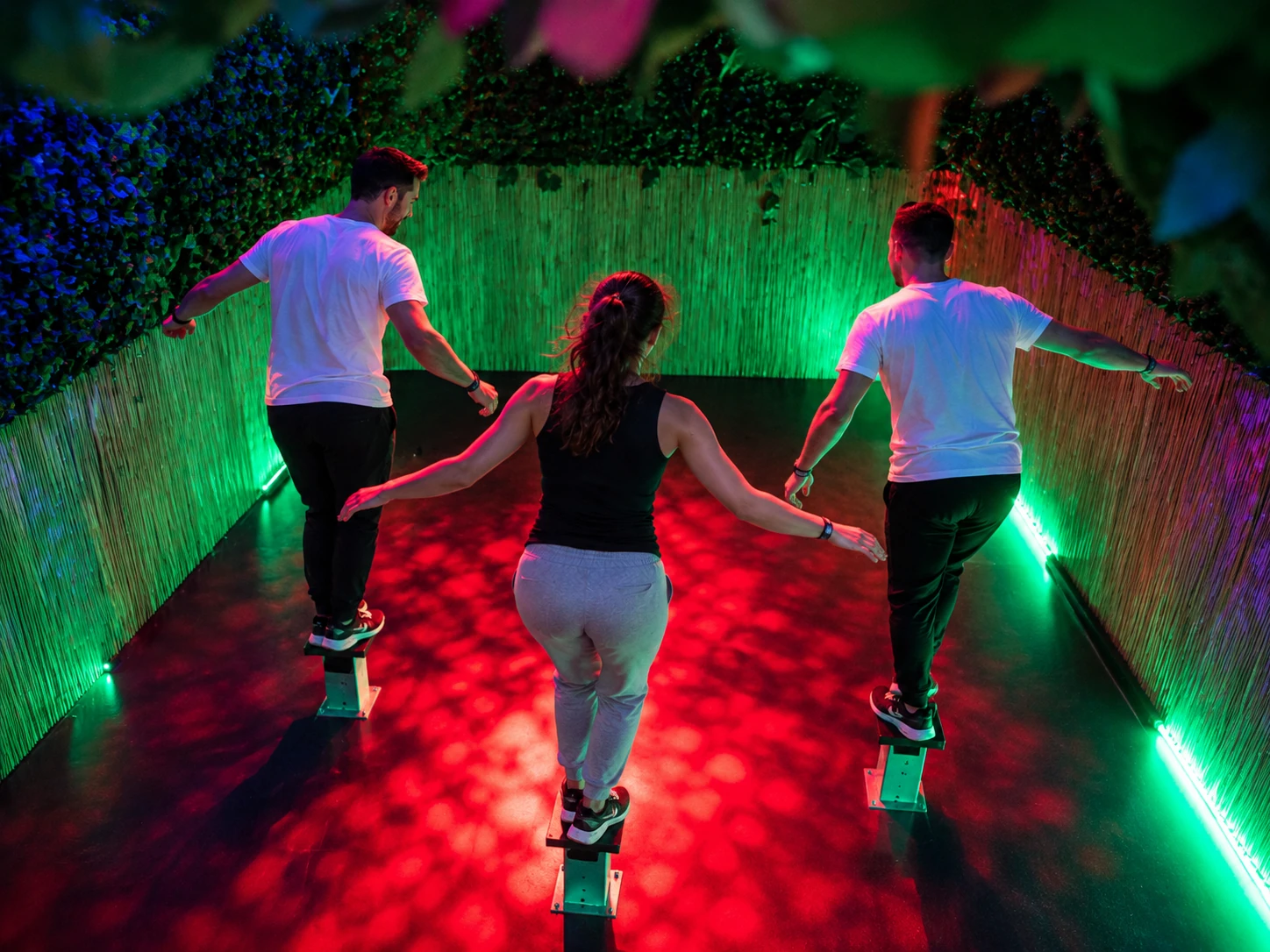 Trois joueurs de dos réalisant un défi d’équilibre dans une salle immersive